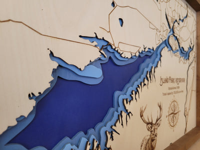 Laser-engraved wood map of Island Park Reservoir featuring blue water inlay lakes and engraved wildlife, with title and other landmarks