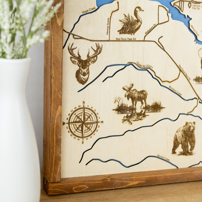 Close-up of Henry's Lake laser-engraved wood map featuring a compass rose, moose, deer, and bear illustrations