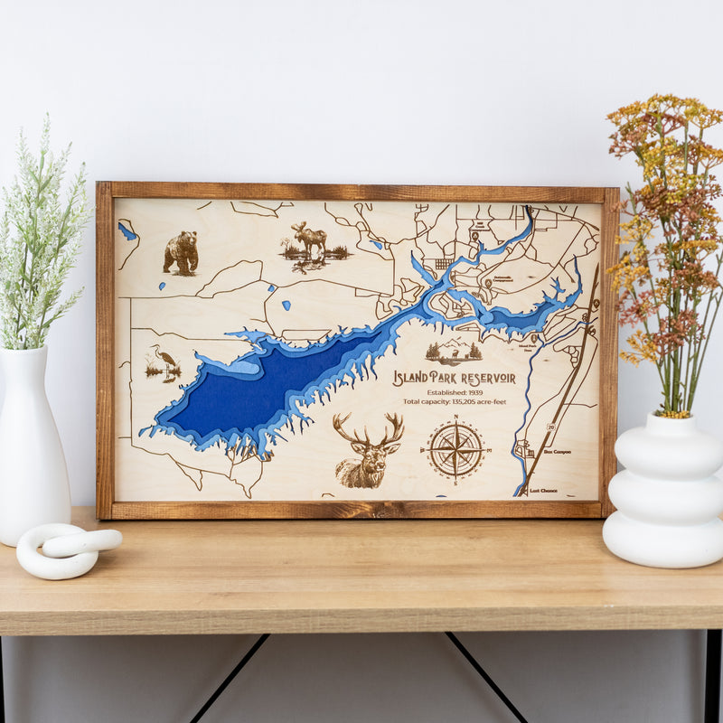 Laser-engraved wood map of Island Park Reservoir featuring lakes, rivers, and engraved wildlife, with labeled trails and landmarks.