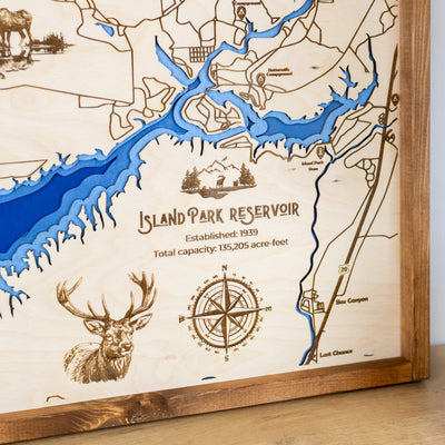 Close up of laser-engraved wood map of Island Park Reservoir featuring the lake, engraved wildlife, compass rose, trail and street names, and other landmarks. 