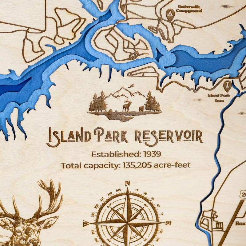 Close up of laser-engraved wood map of Island Park Reservoir featuring the lake, engraved wildlife, compass rose, year established, and lake capacity