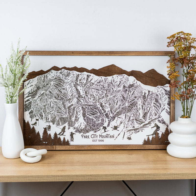 Laser-engraved wooden trail map of Park City Mountain with skier silhouettes and mountain outline, resting on a shelf
