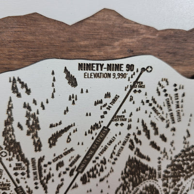 Close-up of a laser-engraved wooden ski trail map showing Ninety-Nine 90, with elevation