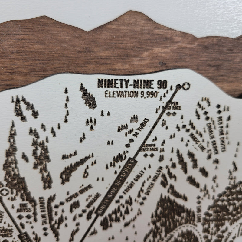 Close-up of a laser-engraved wooden ski trail map showing Ninety-Nine 90, with elevation